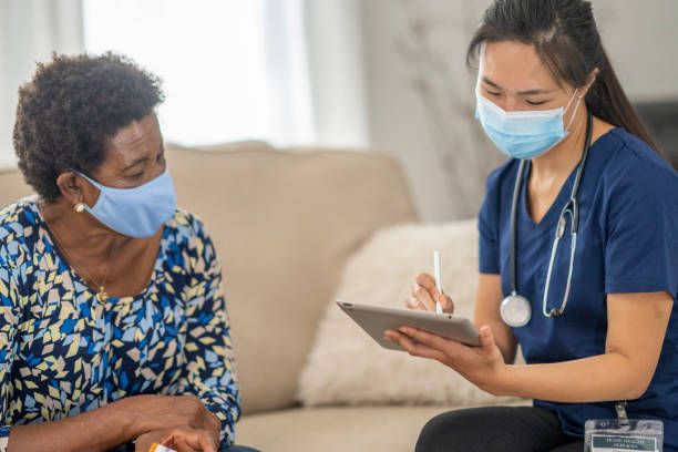 istock Home caregiver visiting with patient wearing masks 1275851212
