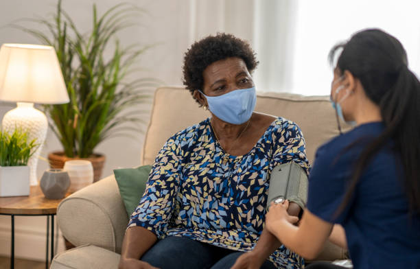 istock Home caregiver visiting with patient wearing masks 1275851216