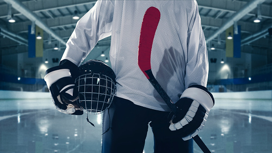 Aspiration. Male hockey player with the stick on ice court background, cropped. Sportsman wearing equipment, preparing for game. Concept of sport, healthy lifestyle, motion, movement, action.
