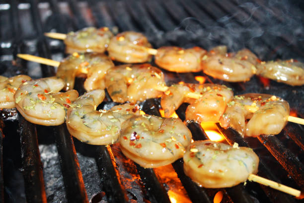Close-up of glazed and seasoned shrimp on skewers being grilled on a barbecue.