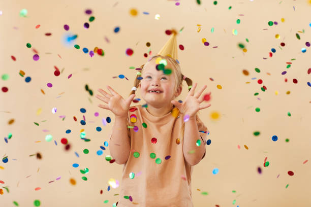 Girl with Down Syndrome Celebrating Birthday at Party Waist up portrait of excited girl with down syndrome smiling happily while standing under confetti shower in studio, copy space dependency photos stock pictures, royalty-free photos & images