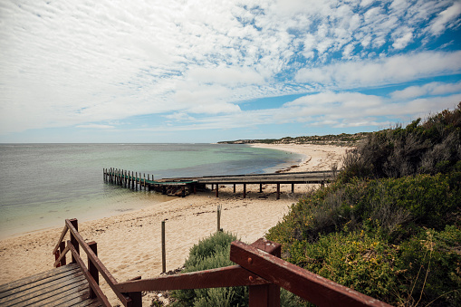 View over a beach in Margaret River, Western Australia. There are steps down to the beach, a boat ramp and a jetty in the image.