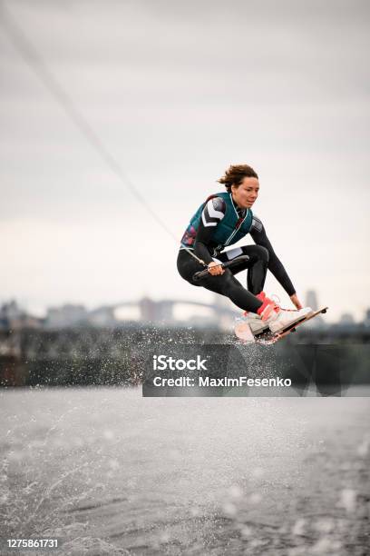 Woman In Wetsuit Holding Rope And Professionally Jumping Over Water On Wakeboard Stock Photo - Download Image Now