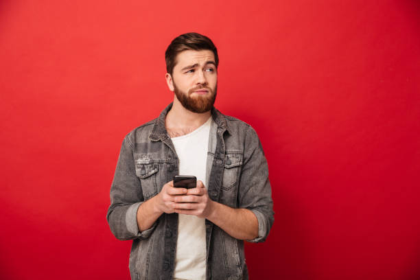 istock Image of Confused bearded man holding smartphone and looking away 1275862025