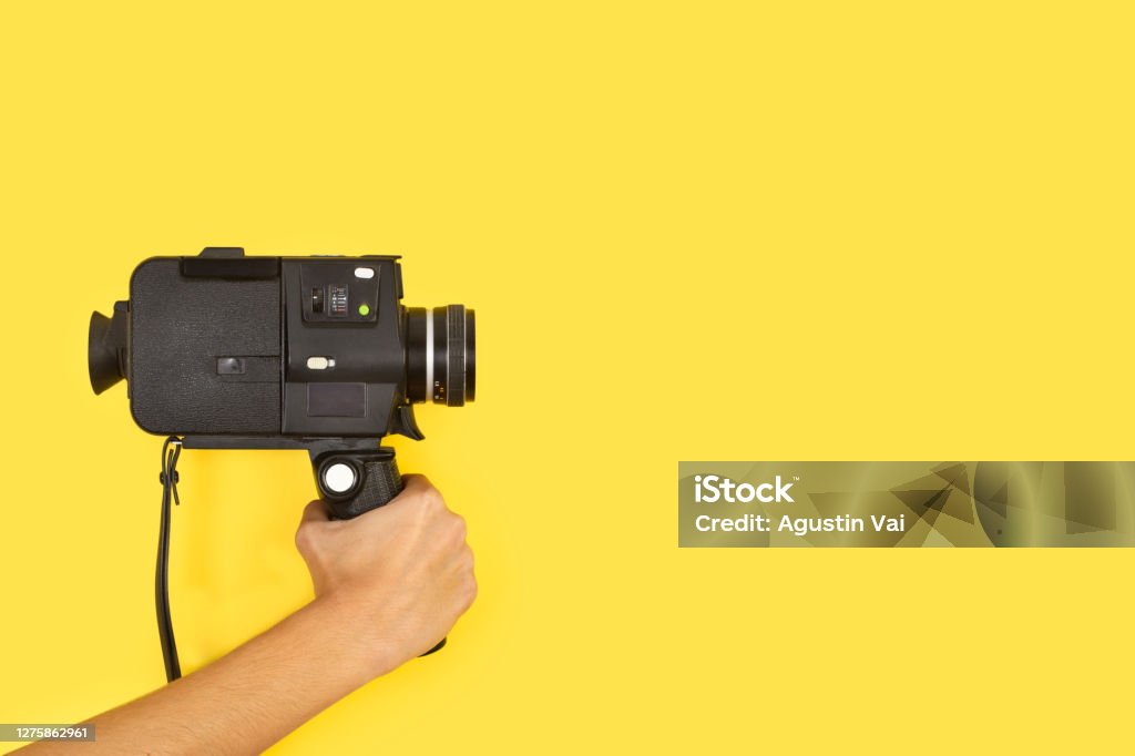 Woman holding an eight mimlimiters camera on a yellow background Woman holding an eight mimlimiters camera on a yellow background with copy space Home Video Camera Stock Photo