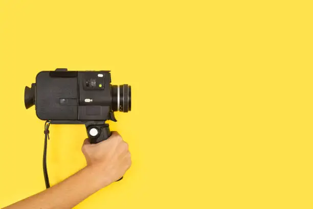 Photo of Woman holding an eight mimlimiters camera on a yellow background