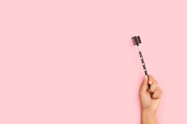 istock Woman hand holding an eyebrow comb on a pink background 1275863097
