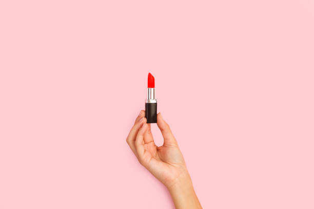 Woman hand holding a red lipstick on a pink background