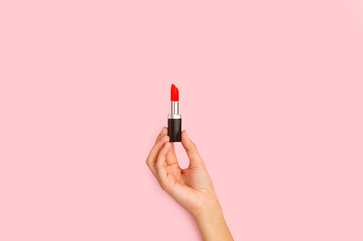 Woman hand holding a red lipstick on a pink background with copy space