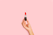 Woman hand holding a red lipstick on a pink background