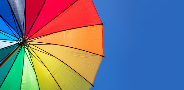 A rainbow of colors are represented in this brightly colored beach umbrella. It is shot from below and there is a blue sky with low cumulus clouds at the bottom.  There is amble copy space. Image is taken from Panama  City Florida on Gulf Coast.