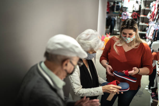 casal sênior usando máscara facial sendo ajudado por uma vendedora enquanto comprava sapatos em um brechó - shoe store sales clerk customer - fotografias e filmes do acervo