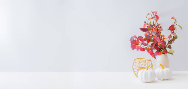 istock Home interior with decor elements. Colorful autumn leaves in a vase on a light background 1275877118