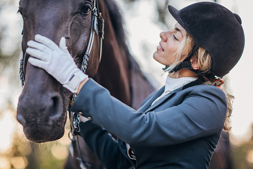 One young beautiful female jockey embracing her horse after training at the riding school.