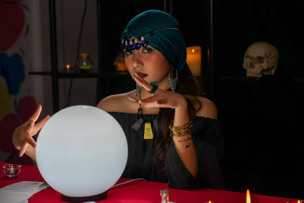 Young pretty Asian woman doing fortume telling witchcraft forecasting the future with crystal ball and Tarot card on red table with black background Young pretty Asian woman doing fortune telling witchcraft forecasting the future with crystal ball and Tarot card on red table with black background asian fortune teller stock pictures, royalty-free photos & images