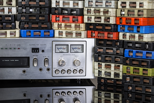 Stacks of 8-track music tapes with a tape deck on a reflective black surface.