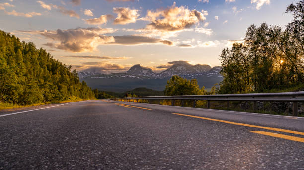 panorama of empty winding country road in norway, europe, scandinavia. auto travel on sunset. blue sky with clouds and mountains. lofoten islands - empty road imagens e fotografias de stock