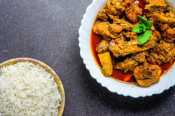 istock Chicken curry or masala , spicy reddish chicken leg piece dish garnished with coriander leaf and arranged in a white ceramic bowl with wooden background 1275880354