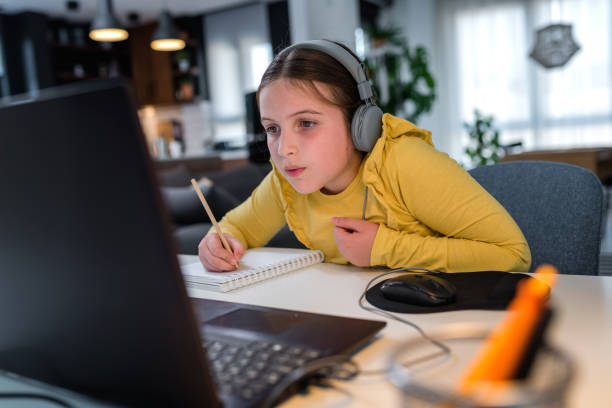istock Cute child with headphones using laptop computer for online learning. Home school. Girl doing homework at home. Lifestyle concept for home schooling. Social distancing and education. 1275880410