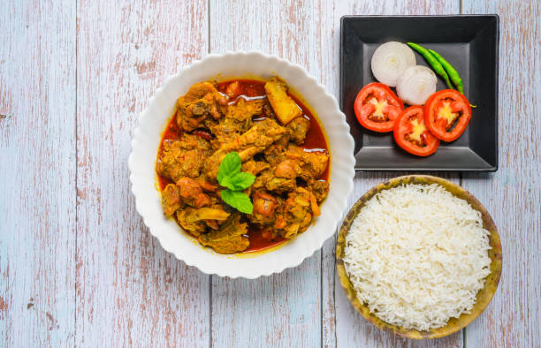 istock Chicken curry or masala , spicy reddish chicken leg piece dish garnished with coriander leaf and arranged in a white ceramic bowl with wooden background 1275880447