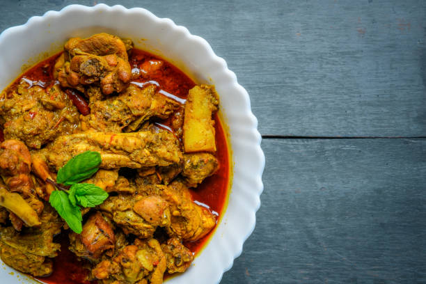 istock Chicken curry or masala , spicy reddish chicken leg piece dish garnished with coriander leaf and arranged in a white ceramic bowl with wooden background 1275881138