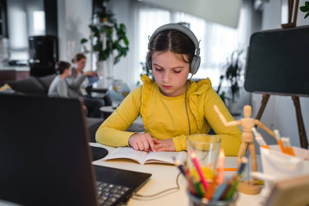istock Cute child with headphones using laptop computer for online learning. Home school. Girl doing homework at home. Lifestyle concept for home schooling. Social distancing and education. 1275881448