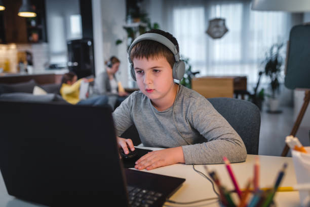 istock Cute boy with headphones using laptop computer for online learning. Home school. Child doing homework at home. Lifestyle concept for home schooling 1275882312