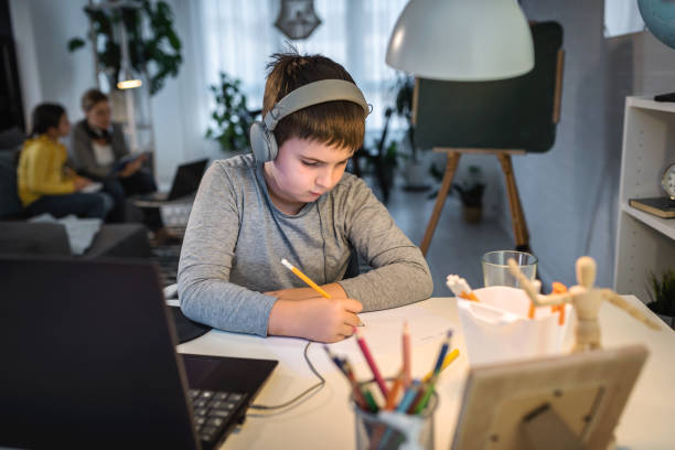 istock Cute boy with headphones using laptop computer for online learning. Home school. Child doing homework at home. Lifestyle concept for home schooling 1275882340