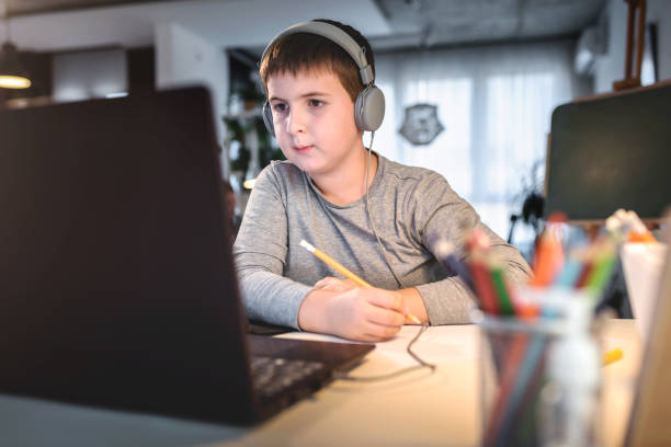 istock Cute boy with headphones using laptop computer for online learning. Home school. Child doing homework at home. Lifestyle concept for home schooling 1275882412