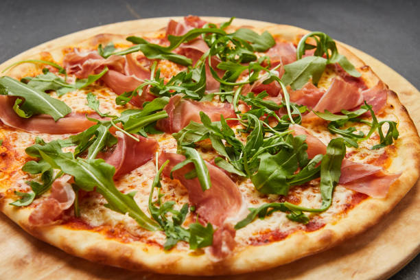 istock Delicious Italian Pizza with Parma ham and arugula, mozzarella cheese on dark background 1275883248
