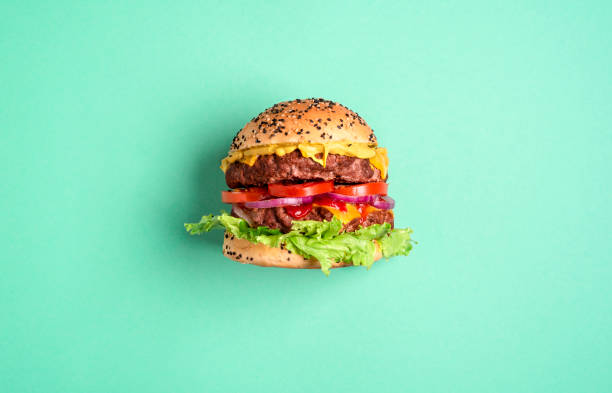 Hamburger on a green background, top view. Burger side view. Homemade burger with double beef patties, cheese, and salad isolated on a green-mint background. Single hamburger side-view comfort food stock pictures, royalty-free photos & images