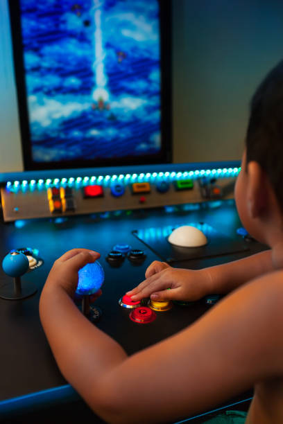 Four year old kid playing retro games on a home arcade with lighted joystick and buttons on a vertical monitor. stock photo