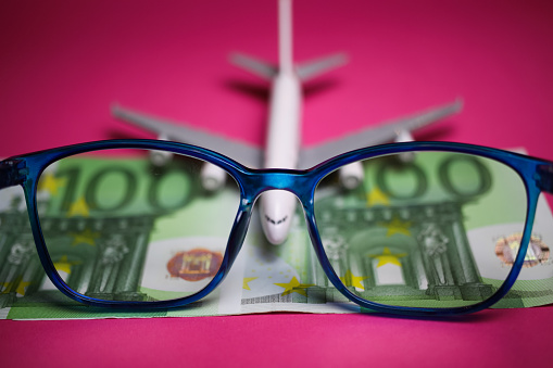 View on isolated eyeglasses with blurred plane and two hundred euro paper banknotes on pink backgound (focus on center of eyeglass frame)