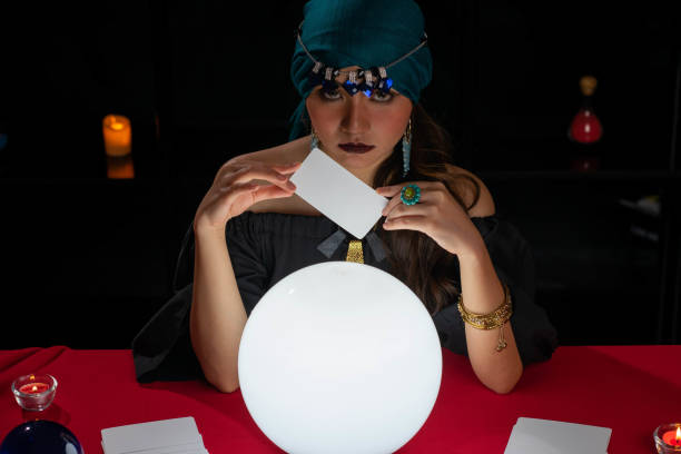 istock Young pretty Asian woman doing fortume telling witchcraft forecasting the future with crystal ball and Tarot card on red table with black background 1275909913