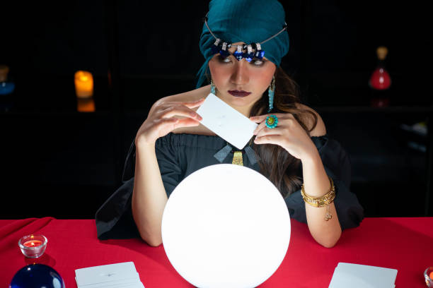 istock Young pretty Asian woman doing fortume telling witchcraft forecasting the future with crystal ball and Tarot card on red table with black background 1275909921