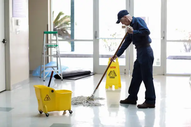 Photo of Senior Adult Janitor mops floor at entry to offices.