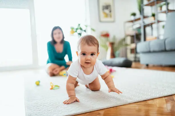 Photo of Mother and baby girl at home, baby crawling and looking for toys
