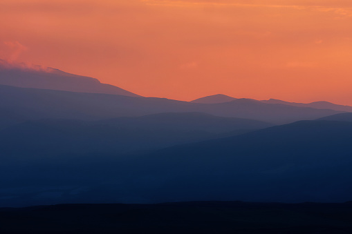 Dramatic blue silhouette of mountain ranges on background of an orange sunset
