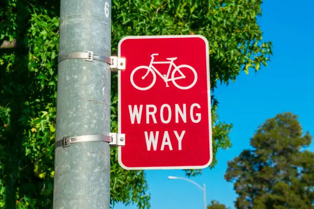 Red bicycle wrong way sign on street pole placed facing wrong-way bicycle traffic.
