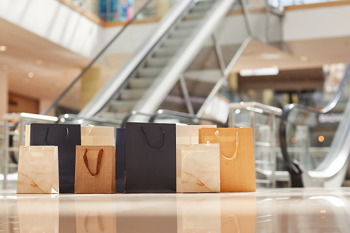 Warm toned image of paper shopping bags on floor in mall with escalator in background, copy space