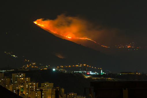 forest fire in the mountains above the city, flames next to houses