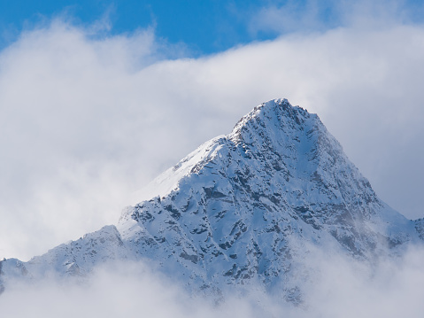 Mountain peak full of snow surronded by clouds in the Alps