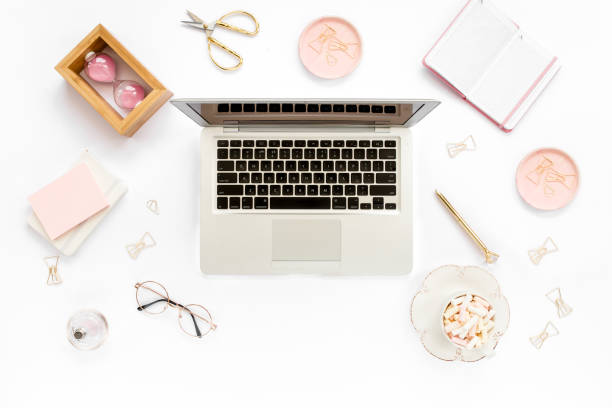 istock Stylized women's home office desk. Workspace with laptop, computer, bouquet ranunculus and roses, clipboard on white background. Flat lay. Top view 1276086537