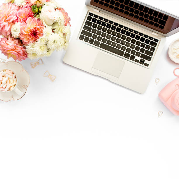 istock Stylized women's home office desk. Workspace with laptop, computer, bouquet ranunculus and roses, clipboard on white background. Flat lay. Top view 1276089753