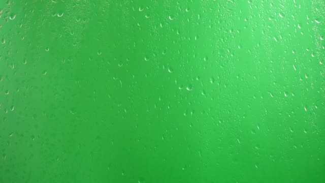 Water drops flow down the glass on a green background.