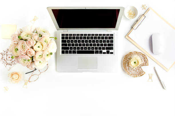 istock Stylized women's home office desk. Workspace with laptop, computer, bouquet ranunculus and roses, clipboard on white background. Flat lay. Top view 1276116481