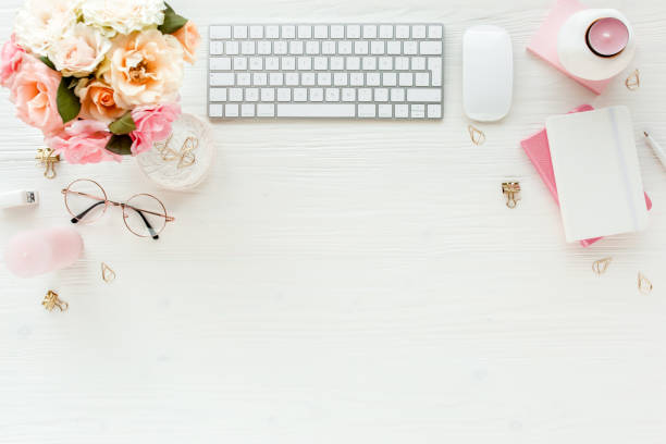 istock Flat lay women's office desk. Female workspace with computer, pink roses flowers, accessories, golden diary, glasses on white background. Top view 1276119832