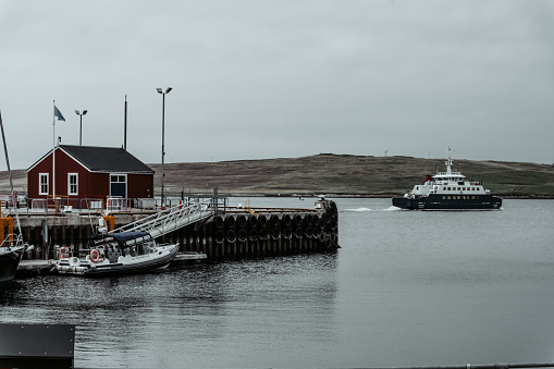 A boat moored in the harbour at Lerwick on a cloudy rainy day, Shetland Islands. In the distance MV Leirna ferry on her way from Lerwick to Bressay.