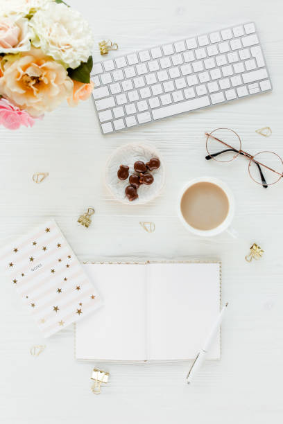 istock Flat lay women's office desk. Female workspace with computer, pink roses flowers, accessories, golden diary, glasses on white background. Top view 1276128355