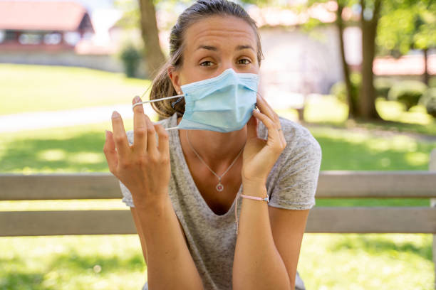 istock Young Woman Removing Her Protective Face Mask in Public Park 1276129415
